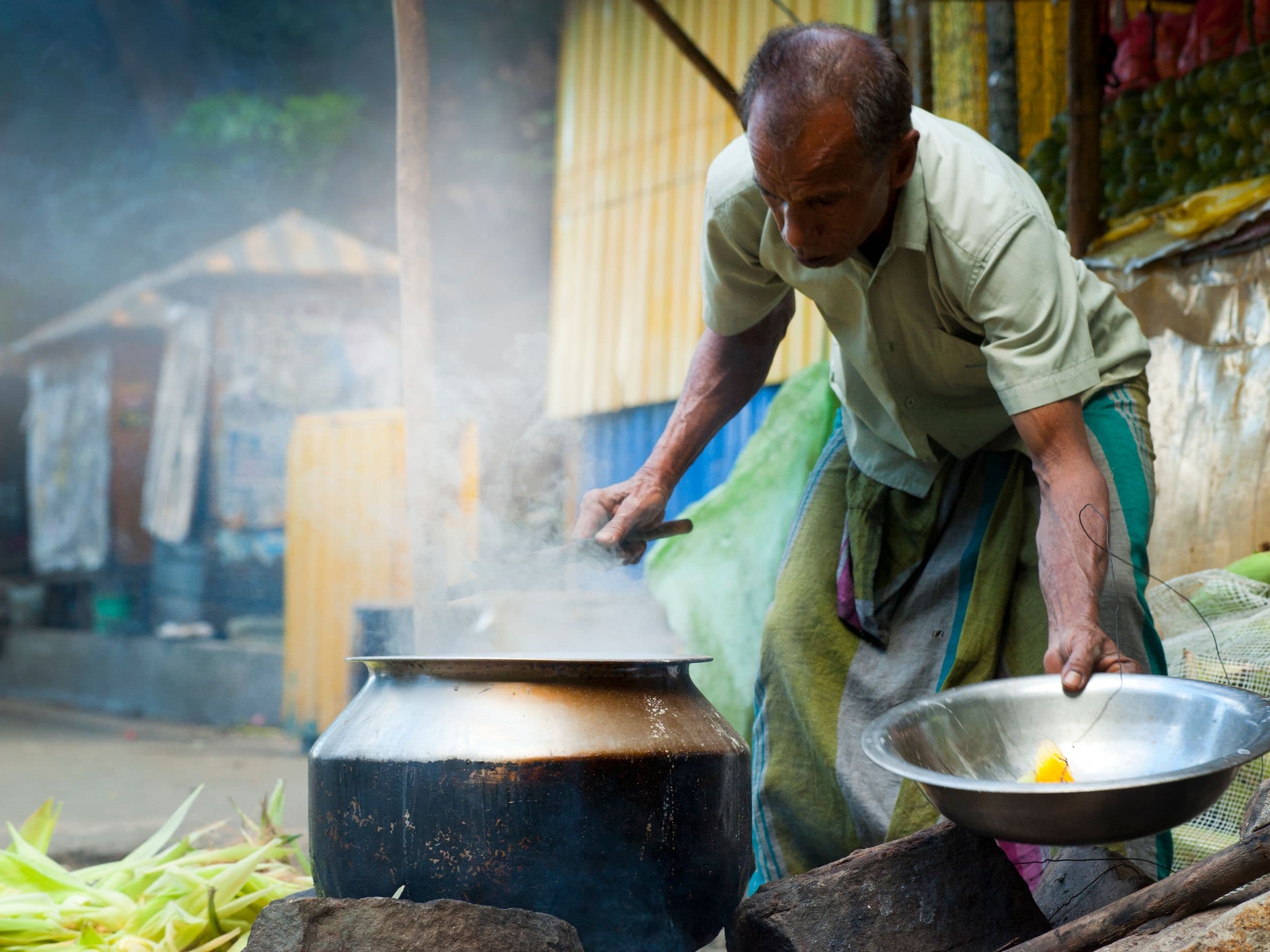 A Sri Lankan cook preparing food over a steaming outdoor pot