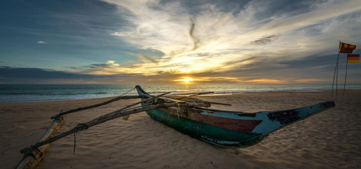 Traditional outrigger boat on an Ahungalla beach at sunset