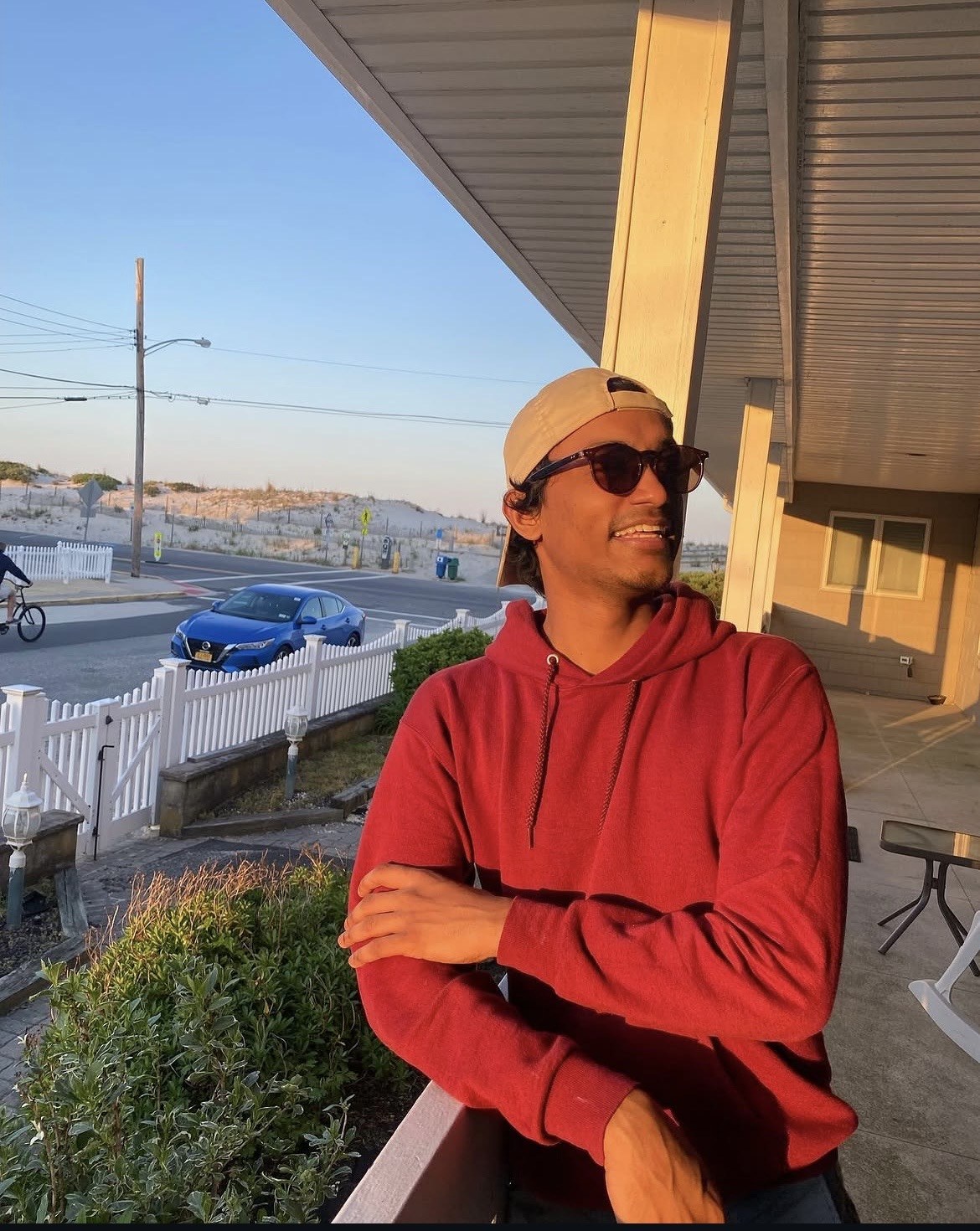 Damshike Piyasena in a red hoodie, leaning on a porch railing
