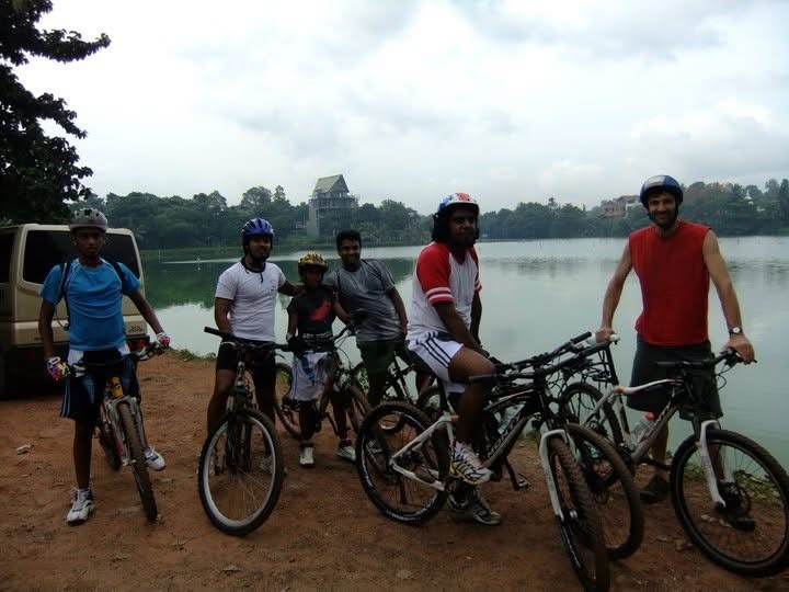 A young group with their bikes beside a lake, helmets on, ready to ride